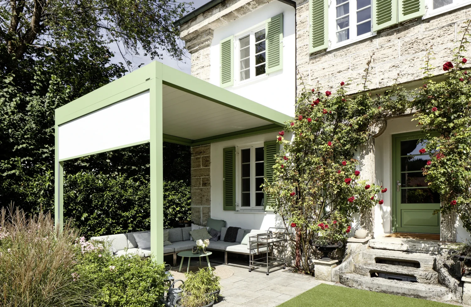 Moderne Terrassenüberdachung mit grünen Fensterläden und blühenden Rosen